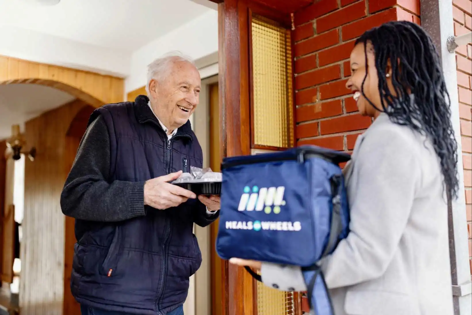 A Meals on Wheels Rockland volunteer handing a meal bag to a senior client at her door.